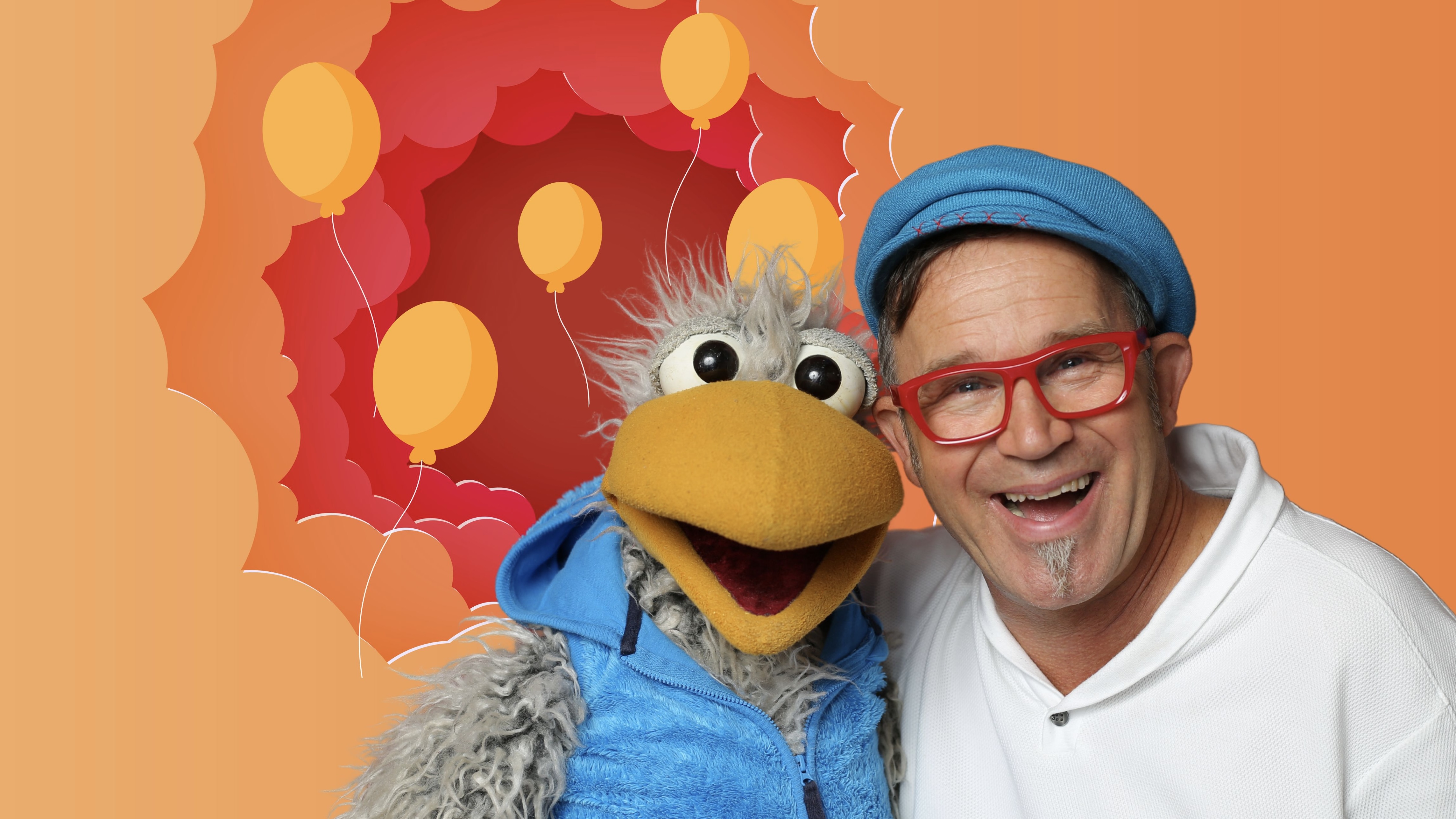 Daniel Kallauch lacht zusammen mit Spaßvogel Willibald vor orangefarbenem Hintergrund mit gemalten Luftballons
